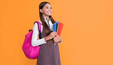 cheerful child with school backpack and workbook on yellow background.