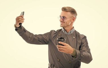 Mutlu gülümseyen iş adamı işadamı resmi ceketli yönetici iş telefonuyla selfie çekiyor. Kahve fincanı stüdyosu beyaz, selfie 'de izole edilmiş..