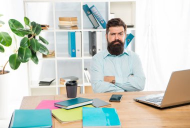 Kendine güvenen, kuşkucu iş adamı. Kollarını çapraz tutuyor. Ofis masasında oturuyor..