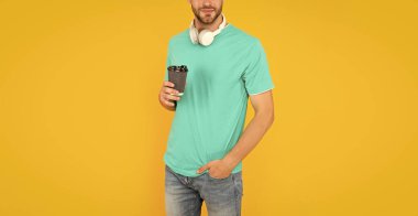 Modern kulaklıklı, kahve bardağıyla kesilmiş bir adam. Online eğitim. Okula dönüyorum. Kulaklıklı genç adam kahve içer. Müzik aşığı. Kablosuz cihaz aksesuarı. yeni teknoloji.