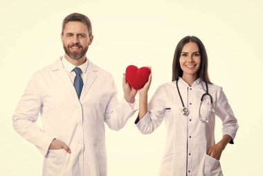 Neşeli kardiyolog stüdyoda kalp bağışı gösterdi. Kalp günündeki kardiyologun fotoğrafı beyaz önlük giyiyor. Steteskoplu kardiyolog. Bağış konsepti. Kalbi olan kardiyolog doktorlar