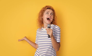 Sarı arka planda izole bir şekilde eğlenen kadın şarkıcı. Genç şarkıcı kadın stüdyoda şarkı söylüyor. Mikrofonlu kadın şarkıcı.