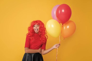 Sarı arka planda helyum balonu olan göz kırpan çocuk..