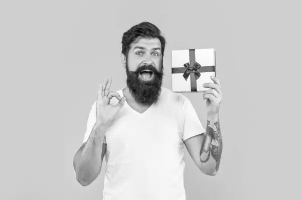 stock image photo of man with present box show ok gesture. man with present box isolated on yellow. man with present box in studio. man with present box on background.