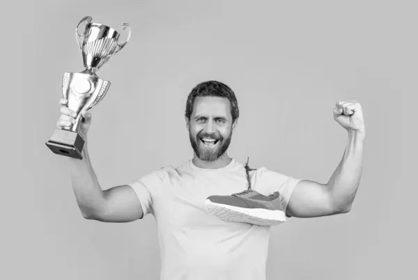 stock image photo of happy champion man hold award and sneakers. champion man hold award isolated on yellow. champion man hold award on background. champion man hold award in studio.