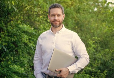 Gülümseyen iş adamının internet işi var. İş adamlarının dışarıda online işleri var. İş adamının bilgisayarında internet işi var. İş adamının fotoğrafı çevrimiçi..