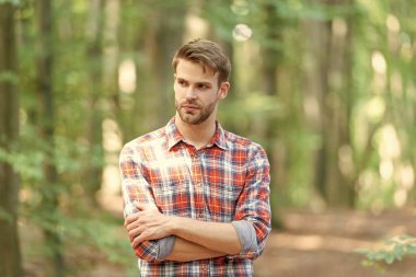 Ormanda beyaz adam tarzında çekilmiş bir fotoğraf. Açık havada beyaz bir adam. Beyaz adamın sakalı var. Kareli gömlek giyen beyaz bir adam..