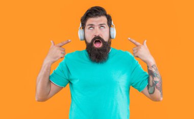 Havalı adam müzik dinleyip sarı ışıkta izole edilmiş parmağıyla işaret ediyor. Havalı kulaklıklı adam müzik dinliyor. Kulaklıklı havalı adamın stüdyo fotoğrafı. Müzik dinliyordum. modern erkek aygıtı.