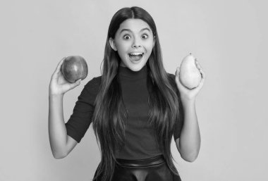 happy amazed child hold fresh apple and pear on yellow background.