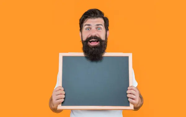 stock image amazed bearded man advertising on blackboard with copy space. bearded man advertising with blackboard isolated on yellow. bearded man hold blackboard for advertising. studio man advertising.