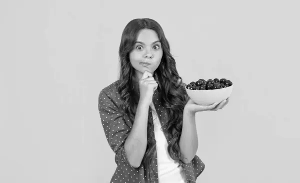 stock image thinking teen girl hold cherry bowl on yellow background.