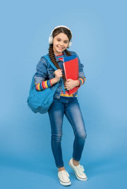 Mutlu genç kız müzik okulunun mavi arka planına gidiyor. Liseli kız kulaklıkla müzik dersi dinliyor. Müzik eğitimi.