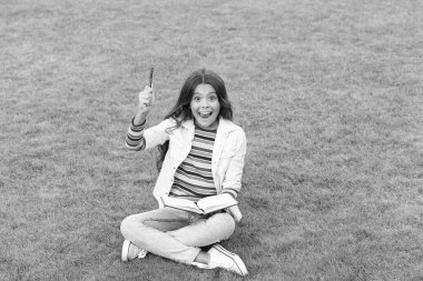 inspired teen girl making notes in notebook sitting on grass. taking notes. student make notes outdoor.