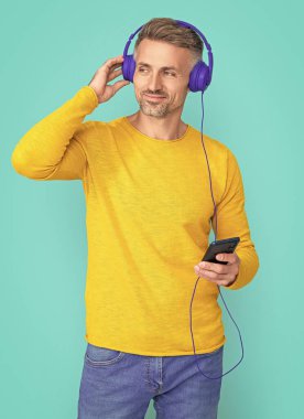 mature man open playlist on mp3 isolated on blue. man open playlist on mp3 at studio. man open playlist on mp3 on background. photo of man open playlist on mp3.