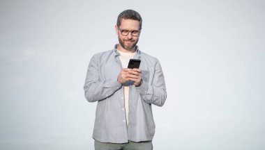 Gözlüklü adam akıllı telefondan mesajla sohbet ediyor. Adam telefonda mesajlaşıyordu. Akıllı telefon iletişimi. Adam gökyüzü arka planında sohbet ediyor.