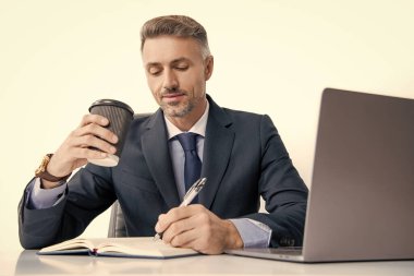 Olgun bir adam iş yerindeki masada yazıyor ve kahve içiyor..