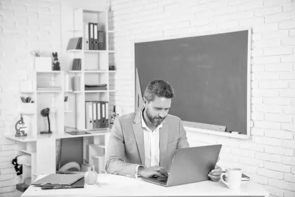 stock image cheerful school teacher in classroom with computer at blackboard.