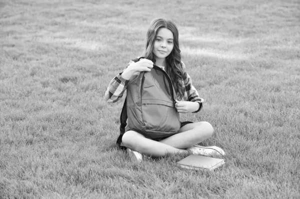 Teen girl opening school bag sitting on grass, education. back to school. pupil at school time.