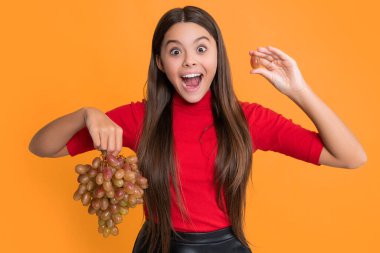 surprised girl hold fresh grapes fruit on yellow background.