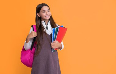 smiling child with school backpack and workbook on yellow background.