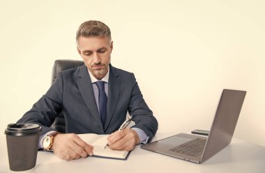 mature manager writing at the table in business office.