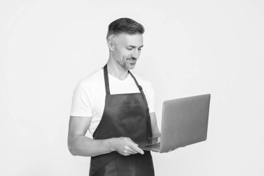 positive mature man in apron chatting on computer.