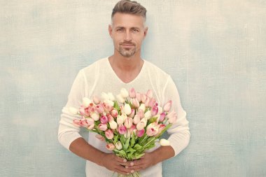 Bahar laleli yakışıklı bir adamın fotoğrafı. Bahar laleli bir adam. Stüdyoda bahar laleleri olan bir adam. Bahar laleleri olan bir adam mavi arka planda izole edilmiş..