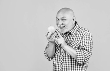 Sarı arka planda elmalı, kareli gömlekli yaşlı adam gülümsüyor..