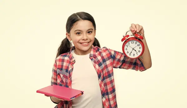 stock image school girl hold alarm clock on background. photo of school girl with alarm clock and homework. school girl with alarm clock isolated on white. school girl with alarm clock in studio.