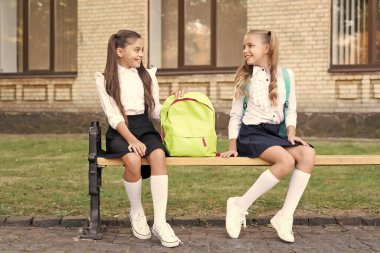 two school girls friends sit on bench with backpack together.