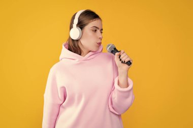 Sarı arka planda mikrofonu olan kulaklıklı genç bir kadın..