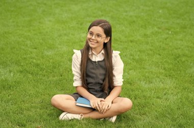 Happy school girl teenager sitting legs crossed on grass. School and education. Back to school.