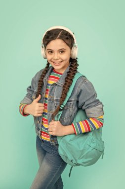 Happy girl giving thumb gesture. Teen girl listening to music blue background. Teenage girl back to school. Non-formal education.