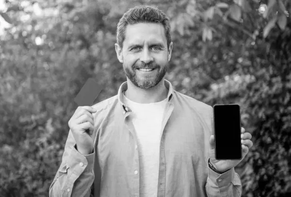 stock image man presenting smartphone screen with copy space on card. photo of man presenting smartphone. man presenting smartphone. man presenting smartphone outdoor.