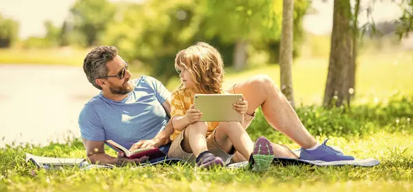 stock image Father and son child relax in park. childhood school education. son with father in summer. family education of father and son kid. Father shapes son education with book tablet. Learning beyond walls.