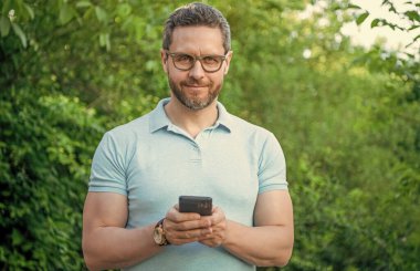 Gülümseyen mutlu adam dışarıda telefonla mesajlaşıyor. Telefonla mesajlaşan ya da e-postaları kontrol eden bir adam. Telefonda mesajlaşan bir adamın fotoğrafı. Telefonda mesajlaşan adam.