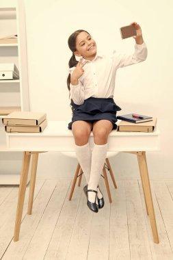 smiling school girl make selfie on phone. photo of school girl make selfie on phone. school girl make selfie in classroom. school girl make selfie at the desk.
