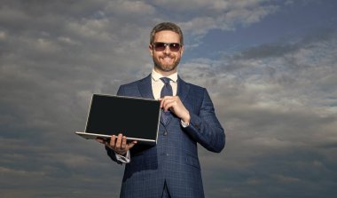 Mutlu adam geliştirici açık dizüstü bilgisayar gösteriyor. Başarılı bir masaüstü geliştiricisi. Yazılım geliştiricisi takım elbise içinde gülümsüyor. Web geliştiricisi gökyüzü arkaplanı, kopyalama alanı.