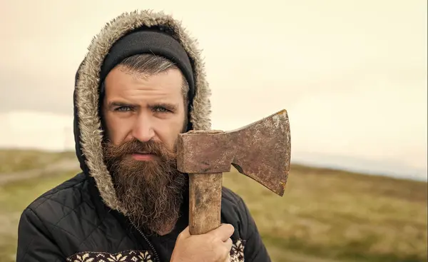 stock image caucasian bearded man lumberjack with axe. photo of bearded man lumberjack holding axe in the mountain. bearded man lumberjack hold axe outdoor. bearded man lumberjack has axe.