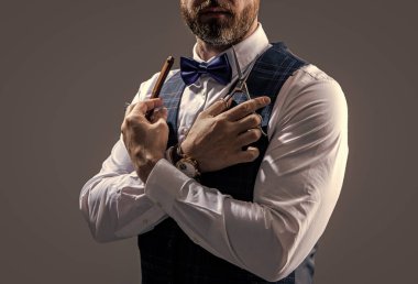 Berber adam gri arka planda izole edilmiş. Makas ve bıçaklı berber. Stüdyodaki berber. Sakallı berberin fotoğrafı..