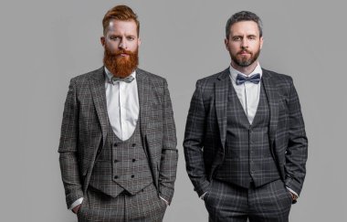 Stüdyoda resmi kıyafet giyen adamların el ele tutuşup ceplerini doldurdukları bir fotoğraf. Resmi takım elbiseli şık erkekler. Smokinli adamlar gri arka planda izole edilmiş. Smokin giymiş iki adam..