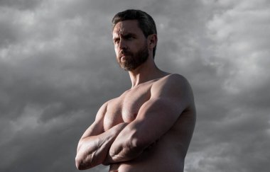 Üstsüz, kaslı adam. Kaslı gövdeli maço bir adam. Gökyüzündeki atletik adam.