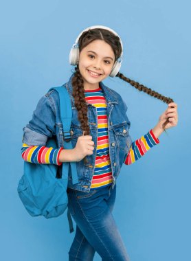 Kulaklıkla müzik dinleyen mutlu genç kız mavi arka plan, eğitim. Gayri resmi eğitim. Okul eğitimi.
