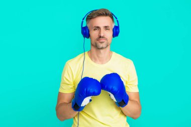 Egzersiz ve yumruk. Boks eldivenli sporcu mavi üzerine izole edilmiş. Kulaklık takan olgun bir boksör. Sporcu boks. Güçlü adam müzik dinler. Spor salonundaki sporcu. Spor giyim sektöründe boksör.