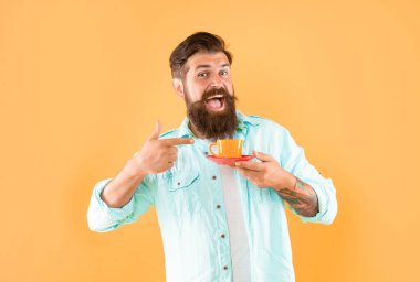 amazed mature hipster with beard pointing finger on coffee cup on yellow background, cappuccino.