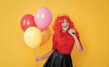 Sarı arka planda mikrofonlu ve parti balonlu mutlu çocuk..