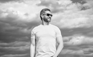 Gökyüzü arka planında sarı gömlekli ve güneş gözlüklü adam..