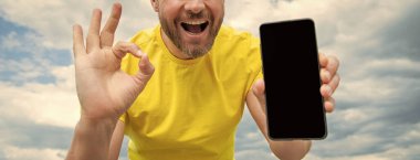 Akıllı telefon ekranı ile fotokopi alanı sunan adamın kırpılmış görüntüsü. Tamam jest gösteriliyor.