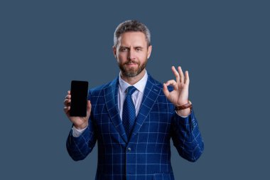 İspanyol iş adamı telefon ekranını sunuyor. Griler 'de izole edilmiş bir telefon gösteren bir iş adamı. Takım elbiseli adam. Yeni telefon uygulaması. Ürünü sunuyorum. İş uygulamasının reklamı. Tamam..