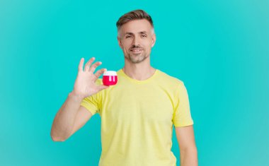 Erkek kozmetik ürünü sunan adam. Mavi renkte yüz kremi gösteren bir adam var. Olgun adam cilt kremi kullanır. Günlük alışkanlık ve kişisel bakım. Cilt güzelliği. Erkek güzellik kozmetiği. Deriyi temizle..